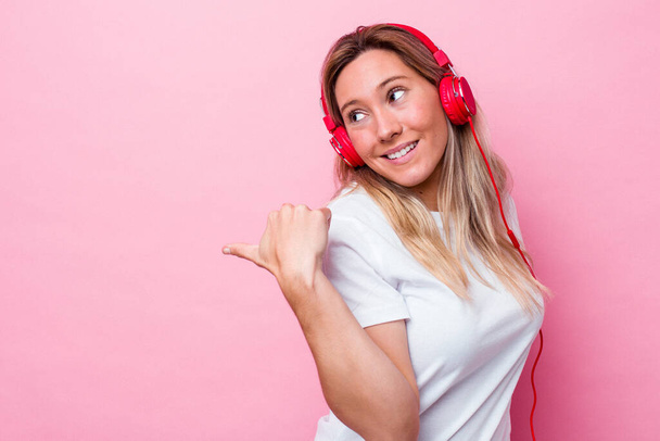 Jeune australienne écoute de la musique isolée sur fond rose points avec pouce loin, riant et insouciant. - Photo, image