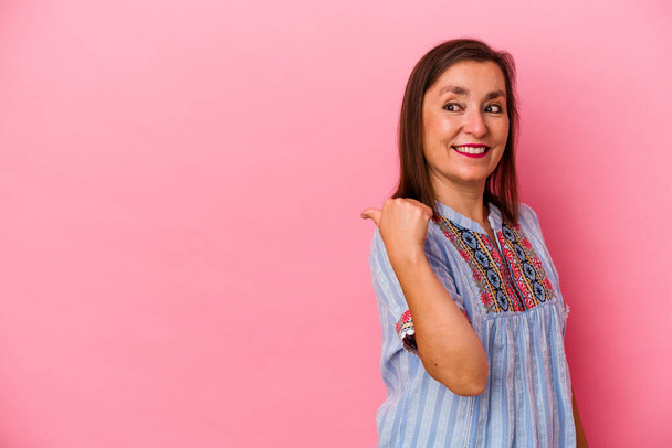 Middle age caucasian woman isolated on pink background points with thumb finger away, laughing and carefree. - Photo, Image