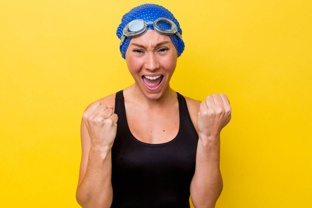 若いオーストラリアの水泳選手の女性は黄色の背景に屈託のない応援と興奮に隔離された。勝利のコンセプト. - 写真・画像