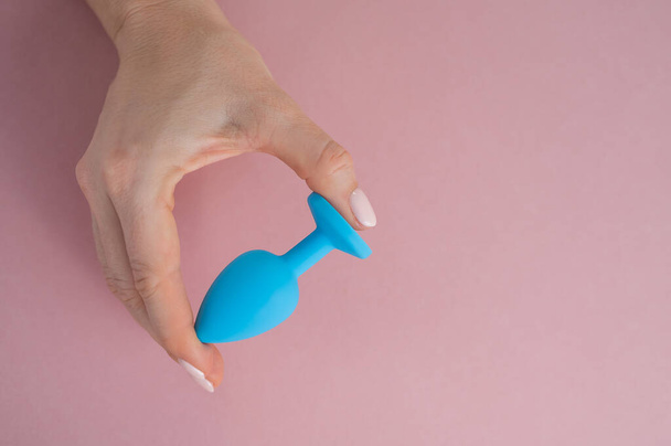 A woman is holding a blue anal plug on a pink background. Adult toy for alternative sex - Фото, изображение