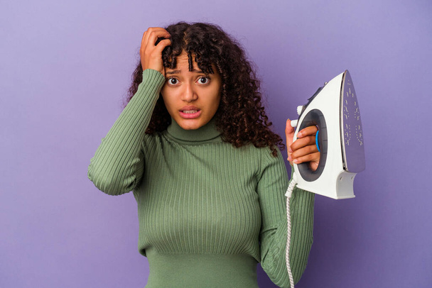 Young mixed race woman holding an iron isolated on purple background being shocked, she has remembered important meeting. - Foto, Imagen