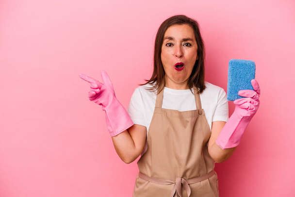 Middle age caucasian woman cleaning home isolated on pink background pointing to the side - Foto, Bild