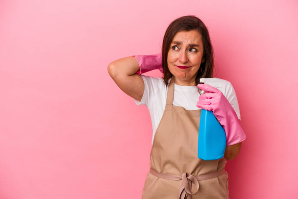Middle age caucasian woman cleaning home isolated on pink background touching back of head, thinking and making a choice. - Фото, зображення