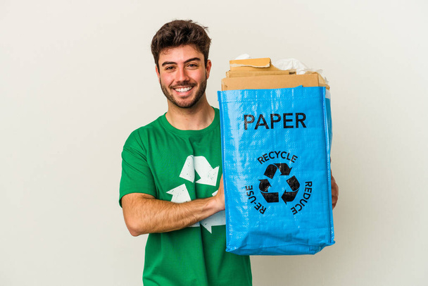 Hombre joven caucásico reciclando cartón aislado sobre fondo blanco riendo y divirtiéndose. - Foto, imagen