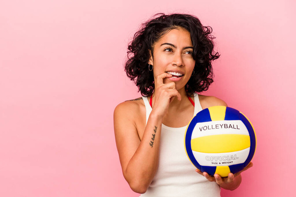 Giovane donna latina in possesso di una pallavolo isolato su sfondo rosa rilassato pensando a qualcosa guardando uno spazio copia. - Foto, immagini