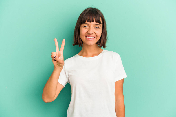 Young mixed race woman isolated on blue joyful and carefree showing a peace symbol with fingers. - Photo, Image
