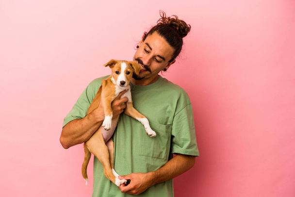 Young caucasian man holding his puppy isolated on pink background - Fotoğraf, Görsel