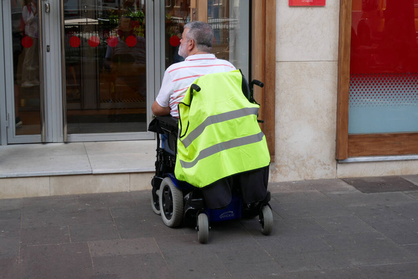 starzec korzystający z wózka inwalidzkiego na ulicy w mieście, człowiek niepełnosprawny może uzyskać dostęp w dowolnym miejscu w miejscu publicznym z wózkiem inwalidzkim sam, na zewnątrz - Zdjęcie, obraz