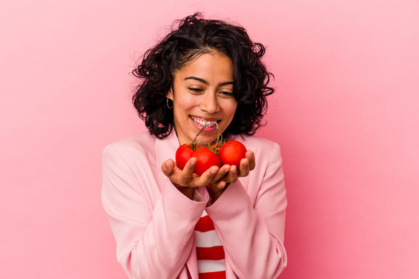 Mujer latina joven sosteniendo tomates aislados sobre fondo rosa - Foto, Imagen