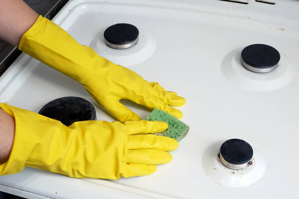 Žena ruce ve žlutých rukavicích mytí plynu sporák v kuchyni s houbičkou, mytí a čištění stěn dlaždice, detailní - Fotografie, Obrázek