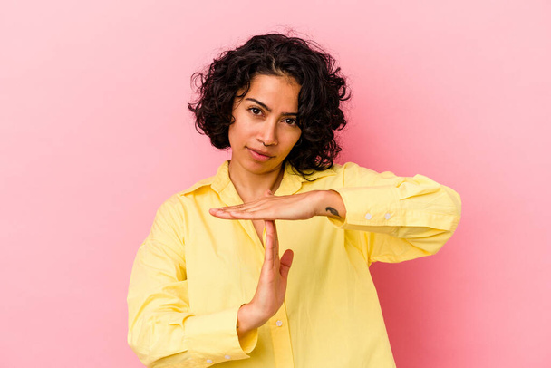 Joven mujer latina rizada aislada sobre fondo rosa mostrando un gesto de tiempo de espera. - Foto, Imagen
