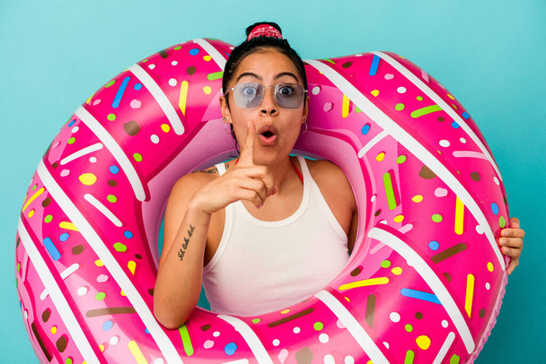 Mavi arka planda izole edilmiş şişirilebilir donut tutan genç Latin bir kadının harika bir fikri var, yaratıcılık kavramı.. - Fotoğraf, Görsel