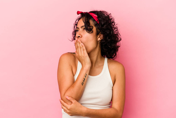 Young curly latin woman isolated on pink background yawning showing a tired gesture covering mouth with hand. - 写真・画像