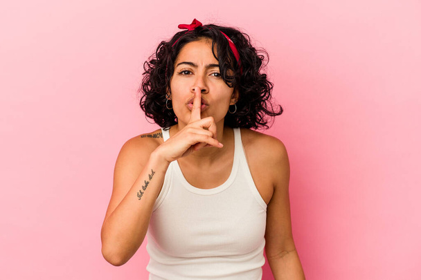 Jovem latina encaracolado isolado no fundo rosa mantendo um segredo ou pedindo silêncio. - Foto, Imagem