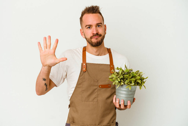 若い庭師入れ墨白地に隔離された植物を保持している白人男性笑顔陽気なショー番号5とともに指. - 写真・画像