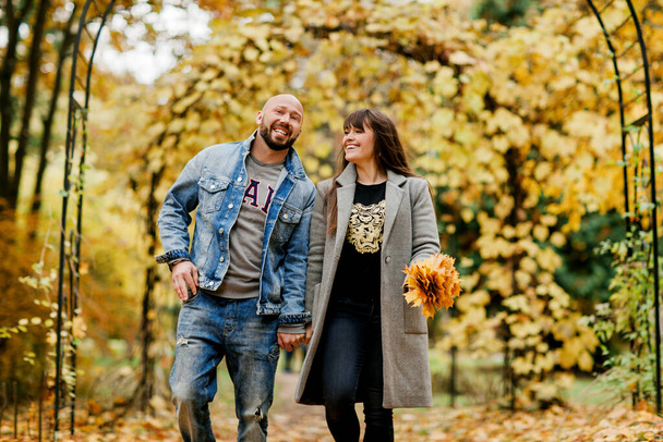 Ein junges Ehepaar spaziert durch den herbstlichen Park, Händchen haltend, ein Mädchen hält einen Strauß Blätter in der Hand. Das Konzept von Beziehungen und Liebe - Foto, Bild