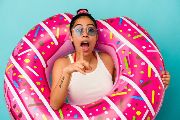 Mavi arka planda izole edilmiş şişme donut tutan genç Latin bir kadın bir fikri var, ilham verici bir kavram.. - Fotoğraf, Görsel