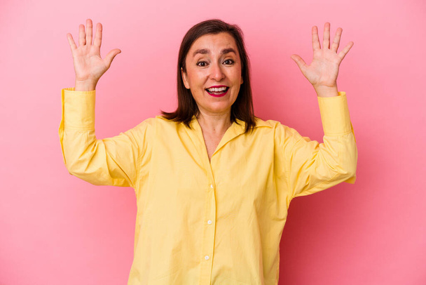 Mujer caucásica de mediana edad aislada sobre fondo rosa recibiendo una agradable sorpresa, excitada y levantando las manos. - Foto, imagen