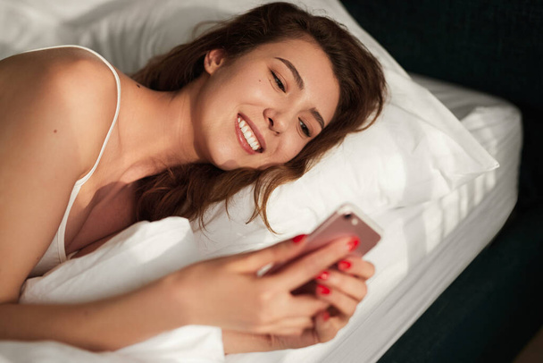 Young woman using smartphone in bed - Φωτογραφία, εικόνα