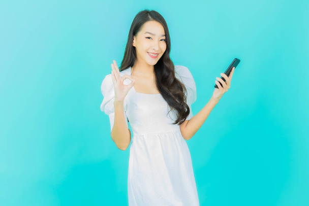 Muotokuva kaunis nuori aasialainen nainen hymyilee älykkäällä matkapuhelimella väritaustalla - Valokuva, kuva