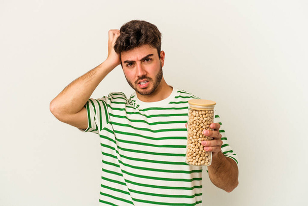 Young caucasian man holding chickpeas jar isolated on white background being shocked, she has remembered important meeting. - Foto, immagini