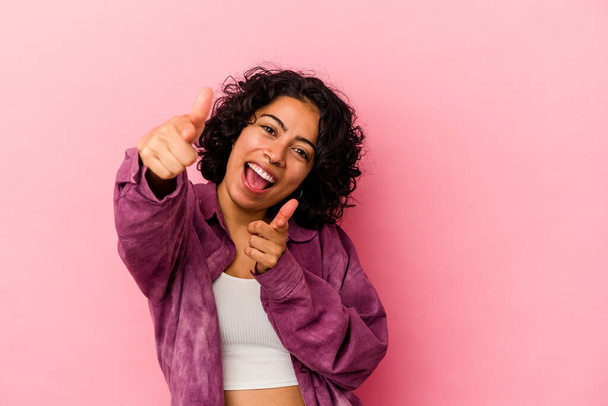Joven mujer latina rizada aislada sobre fondo rosa sonrisas alegres apuntando al frente. - Foto, Imagen