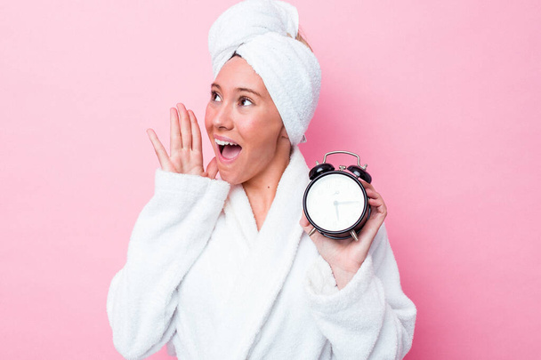 Młoda australijska kobieta opuszcza prysznic późno odizolowana na różowym tle krzycząc i trzymając dłoń blisko otwartych ust. - Zdjęcie, obraz