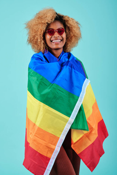 Afro mulher sorrindo enquanto envolto em uma bandeira do arco-íris para apoiar a comunidade LGBTQ. - Foto, Imagem