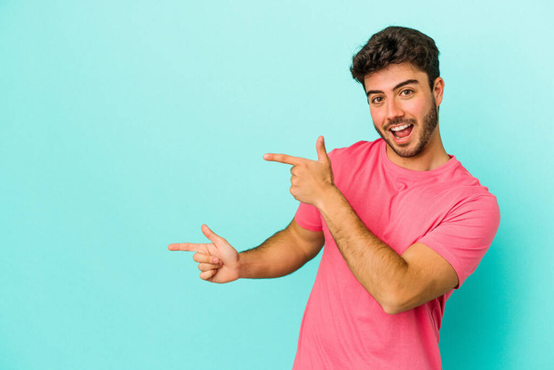 Young caucasian man isolated on blue background excited pointing with forefingers away. - Photo, Image