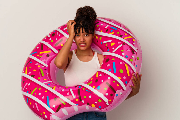 Joven mujer de raza mixta sosteniendo un donut inflable de aire aislado sobre fondo blanco siendo sorprendido, ella ha recordado reunión importante. - Foto, imagen
