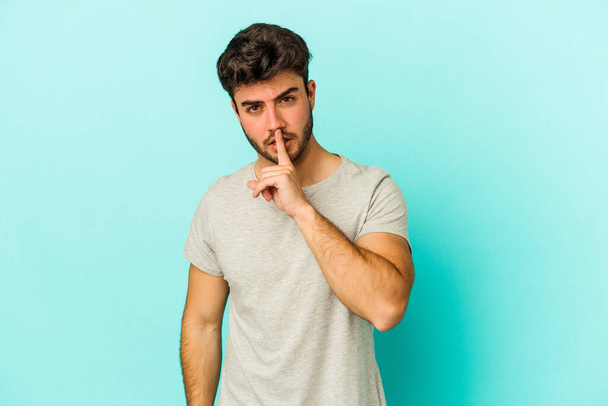 Young caucasian man isolated on blue background keeping a secret or asking for silence. - Photo, Image