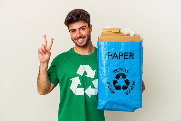 Jonge blanke man recycling karton geïsoleerd op witte achtergrond tonen nummer twee met vingers. - Foto, afbeelding