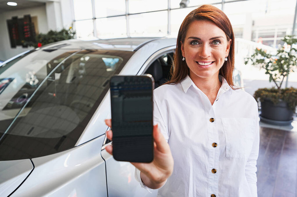 Contented car showroom employee demonstrating her gadget - Photo, Image