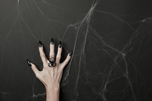 Hand with long black nails and spider ring on a black background with cobwebs. Happy Halloween holiday concept. - Foto, Bild