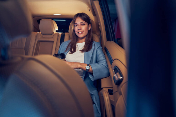 Radostná žena s šálkem kávy sedí v autě - Fotografie, Obrázek