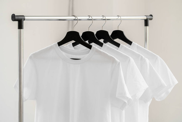Row of white t-shirts on hangers on rack - Fotó, kép
