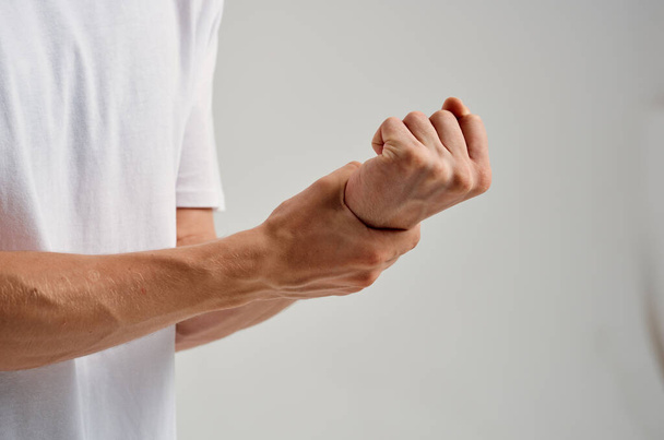 a man in a white t-shirt holding a hand pain in the wrist - Foto, imagen