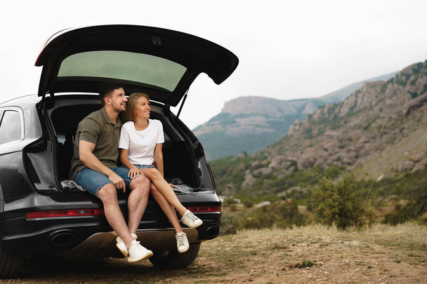 Young happy couple on a road trip sitting in car trunk - Foto, immagini