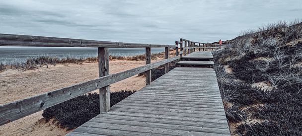 A wooden boardwalk on an elevated grassy coast under a cloudy sky - Photo, image