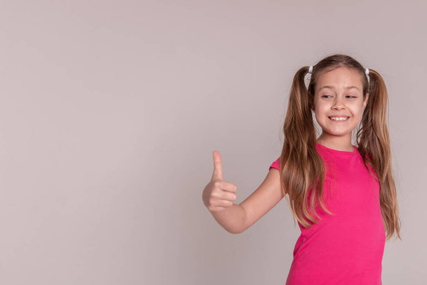 a sporty beautiful girl with tails in pink clothes shows her finger up. on isolated white background. Copy space - Φωτογραφία, εικόνα