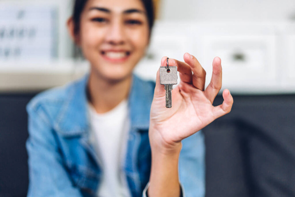 Junge aufgeregte glückliche asiatische Frau hält neuen Hausschlüssel in den Händen und kauft ein neues Zuhause und zieht um. Geschäfts- und Immobilienkonzept - Foto, Bild