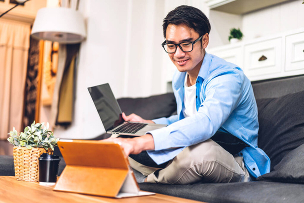 Mladý usměvavý asijský muž pomocí notebooku pracovní a video konference on-line setkání s kolegy doma. Mladý kreativní muž použít tablet.work z domova koncept - Fotografie, Obrázek