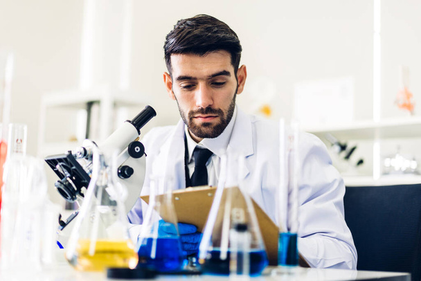 Ammattimainen tiedemies mies tutkimus ja työskentely tekee kemiallisen kokeen samalla analysoimalla ja sekoittamalla nestettä koeputkessa. - Valokuva, kuva