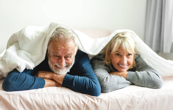 Portrait of smiling senior happy couple relaxing and talking together on bed at home.Elderly husband and wife looking at camara.Retirement couple concept - Photo, image