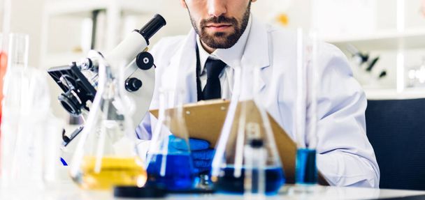 Επαγγελματίας επιστήμονας άνθρωπος έρευνα και την εργασία που κάνει ένα χημικό πείραμα, ενώ κάνει την ανάλυση και ανάμειξη υγρού σε δοκιμαστικό σωλήνα.Νεαρός επιστήμονας άνθρωπος που αναζητούν χημική ουσία δείγμα στο γυαλί στο εργαστήριο - Φωτογραφία, εικόνα