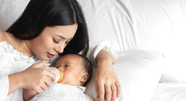Muotokuva nauttia onnellinen rakkaus perhe aasialainen äiti leikkii suloinen pieni aasialainen baby.Mom ruokinta pullo maitoa söpö poika valkoinen makuuhuone. - Valokuva, kuva