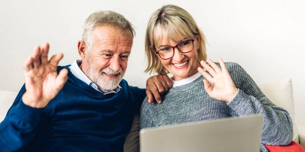 一緒にラップトップコンピュータを使用して楽しい時間を過ごしているシニア夫婦。幸せな高齢者の夫と妻ソーシャルメディアをチェックし、自宅でソファに座っている間にニュースやショッピングをオンラインで読む - 写真・画像