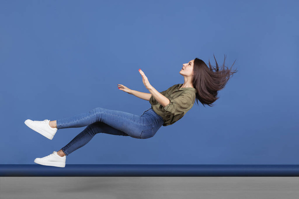 Immagine orizzontale a figura intera di giovane ragazza che cade isolata su sfondo blu. Levitazione sognante - Foto, immagini