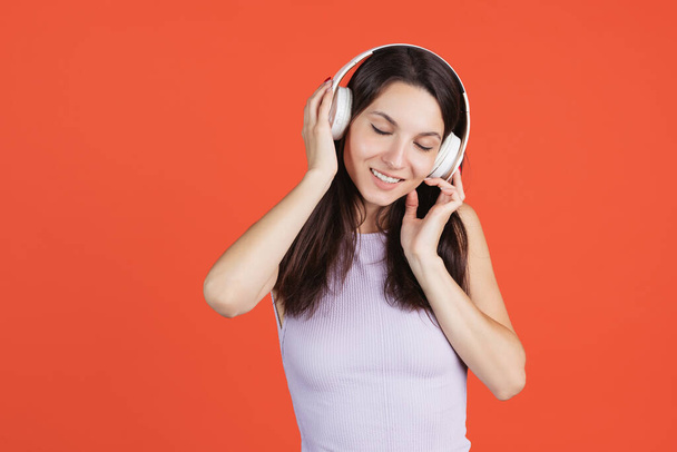 Portrait of young beautiful woman in headphones isolated over red background - Photo, image