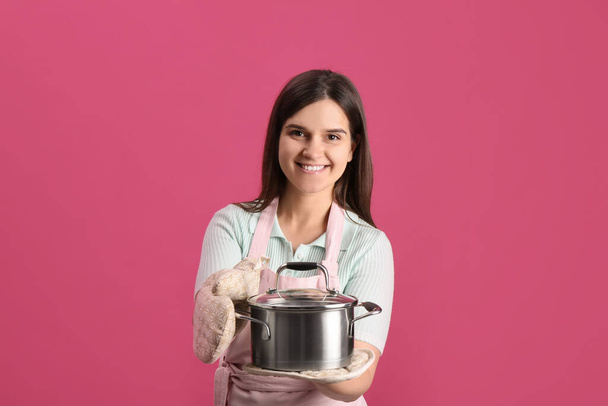 Happy young woman with cooking pot on pink background - Photo, Image